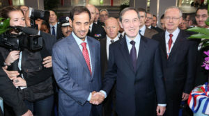Two men in suits shaking hands in a formal setting.