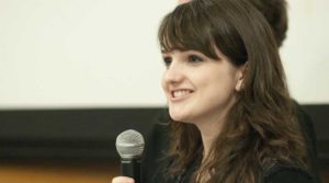 A woman speaking into a microphone with a friendly expression.