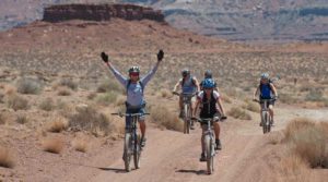 Two cyclists raising arms in celebration on a desert trail.