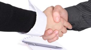 Two people shaking hands over a document and pen, symbolizing agreement.