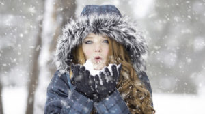 Woman in winter coat blowing snow from her hands.