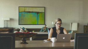 Woman working on laptop at a desk with coffee and snacks.