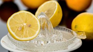 A glass lemon squeezer with fresh lemon halves.