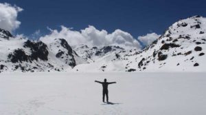 Person standing with arms outstretched on snowy mountain landscape under blue sky.