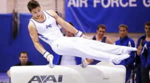 Male gymnast performing on pommel horse during competition.