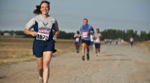 A smiling runner leads a race on a gravel path with competitors behind.