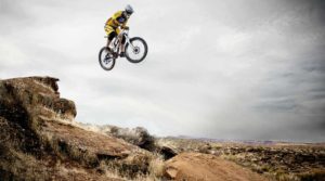 Mountain biker mid-air during a jump over rocky terrain.