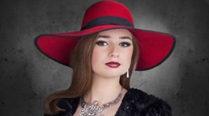 Woman wearing a large red hat and elegant jewelry.