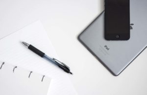 Workspace with a pen, paper, and a laptop corner on a white desk.