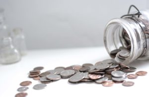 Coins spilling out of a tipped jar onto a white surface.