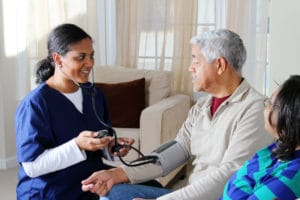 Nurse checking elderly man's blood pressure at home.