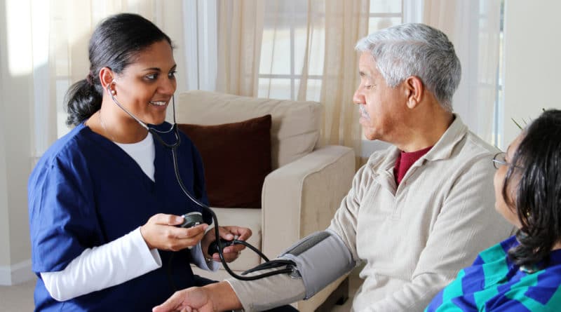 Nurse checking elderly man's blood pressure at home.