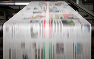 Newspapers rapidly moving through a printing press.