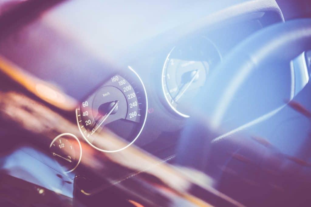 Blurred close-up of a car dashboard with speedometer and steering wheel.