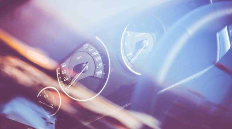 Blurred close-up of a car dashboard with speedometer and steering wheel.