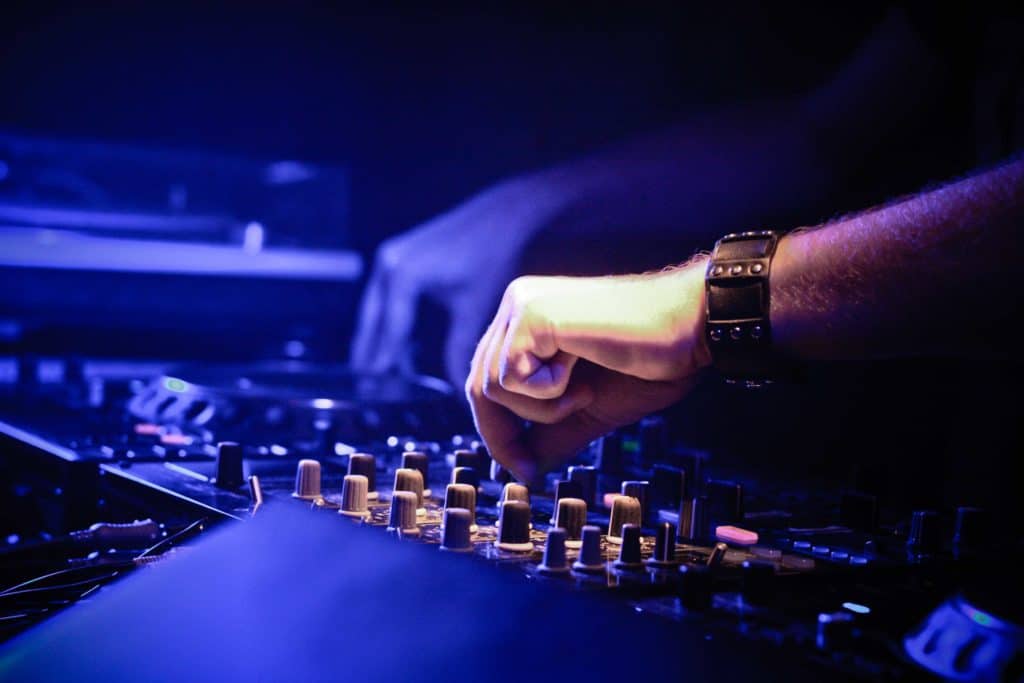 DJ adjusting controls on a professional mixer in a dimly lit club.