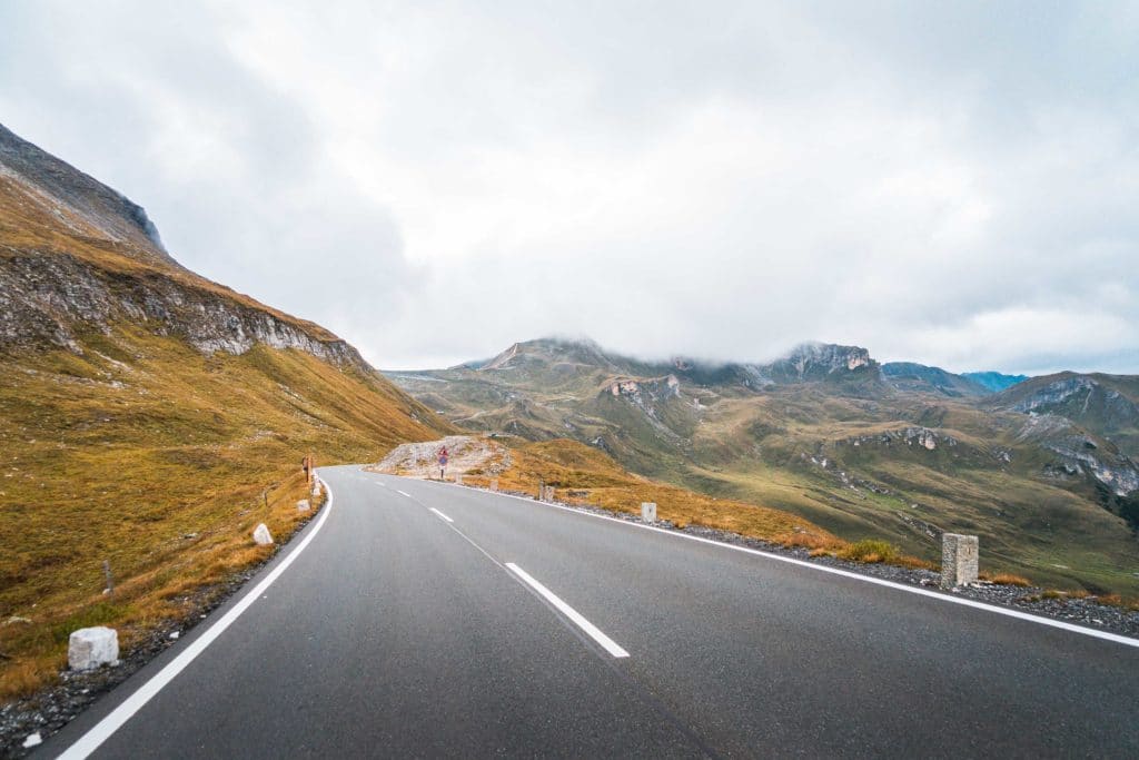 Empty winding mountain road under a cloudy sky.