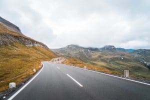 Empty winding mountain road under a cloudy sky.