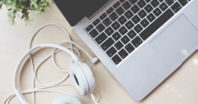 White headphones beside a laptop keyboard on a wooden desk.