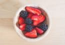 A bowl of strawberries and blackberries on a light wooden surface.
