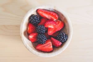 A bowl of strawberries and blackberries on a light wooden surface.