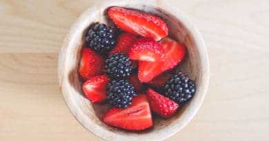 A bowl of strawberries and blackberries on a light wooden surface.