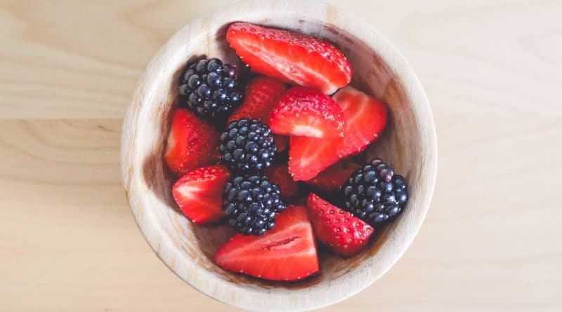 A bowl of strawberries and blackberries on a light wooden surface.
