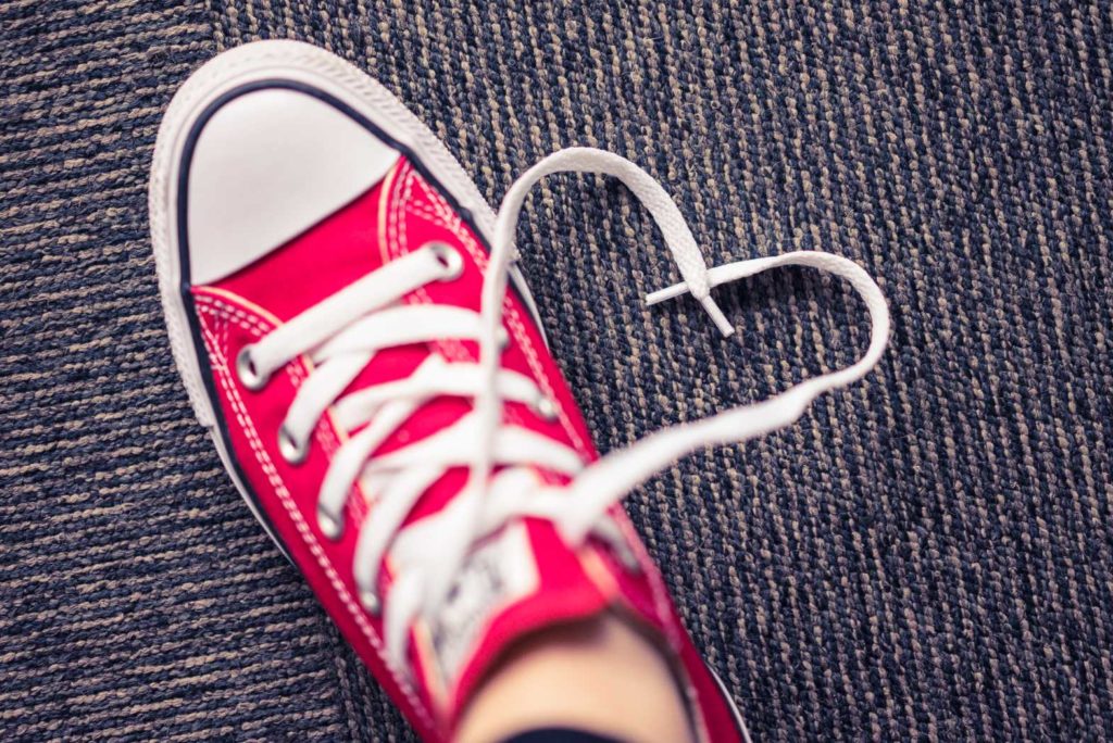 Red sneaker with heart-shaped shoelace on carpet.