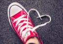 Red sneaker with heart-shaped shoelace on carpet.