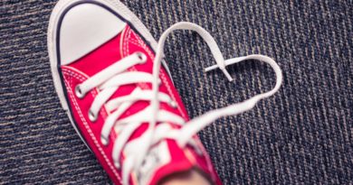 Red sneaker with heart-shaped shoelace on carpet.