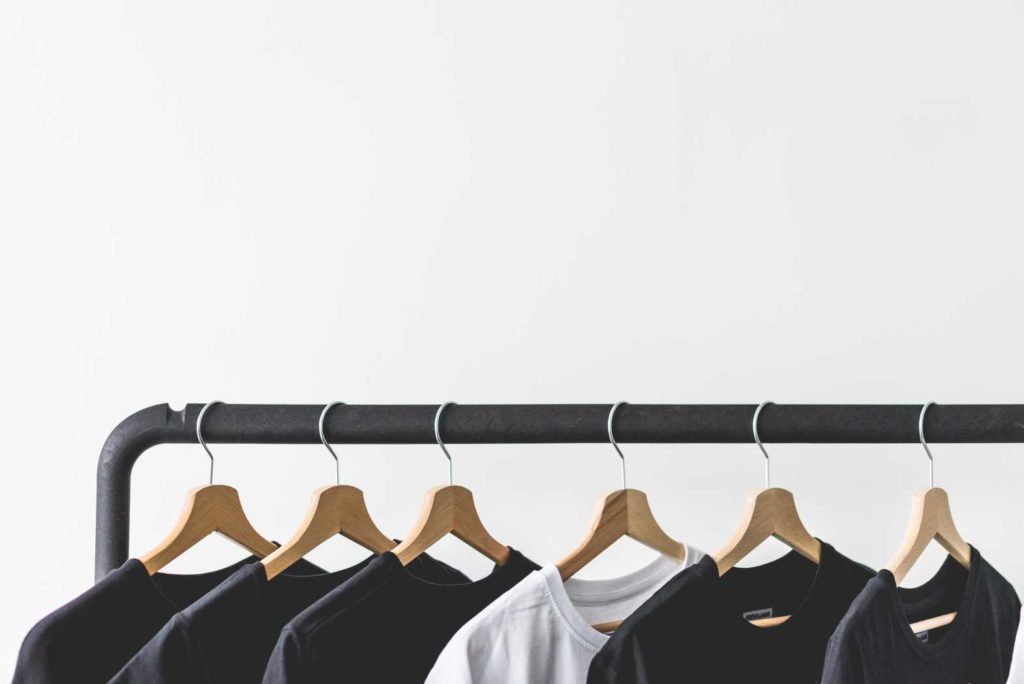 Black and white t-shirts hanging on wooden hangers on a clothing rack.