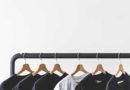 Black and white t-shirts hanging on wooden hangers on a clothing rack.