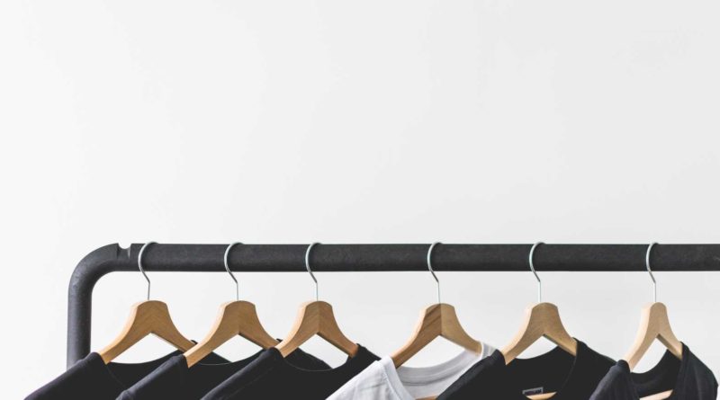 Black and white t-shirts hanging on wooden hangers on a clothing rack.