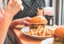 A person eating a burger with fries on a white plate.