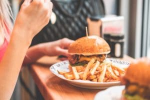 A person eating a burger with fries on a white plate.
