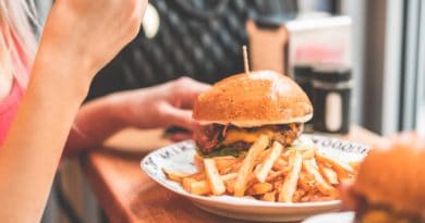 A person eating a burger with fries on a white plate.