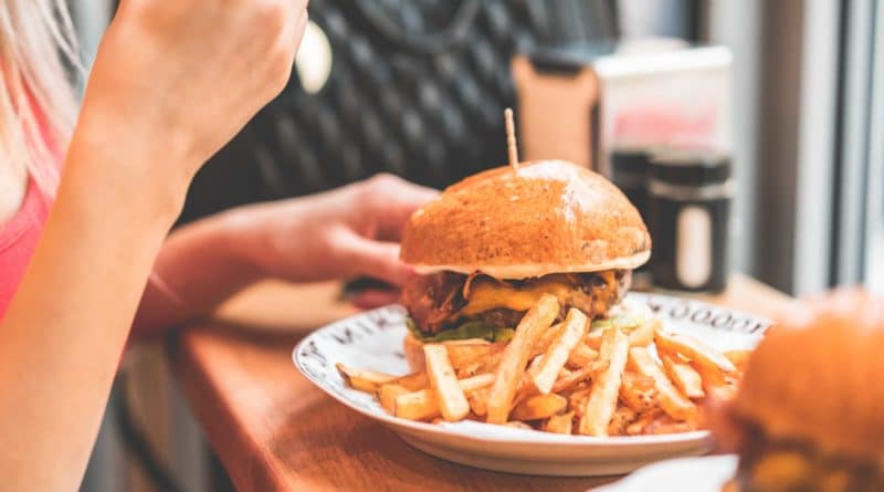 A person eating a burger with fries on a white plate.