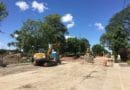 Construction site with excavator working on a dirt road under a blue sky.