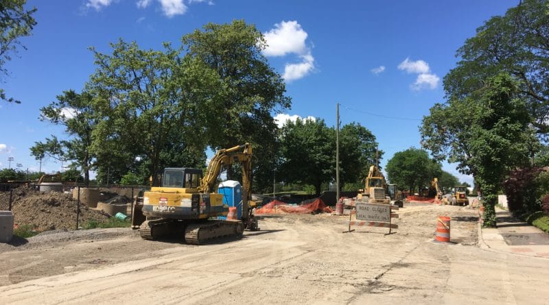 Construction site with excavator working on a dirt road under a blue sky.