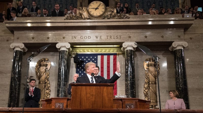 A man speaking at a podium in a formal government setting with an American flag behind.