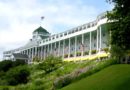 Historic Grand Hotel with a large veranda and American flags on a sunny day.