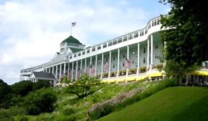 Historic Grand Hotel with a large veranda and American flags on a sunny day.