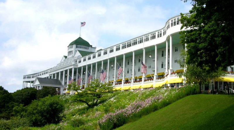 Historic Grand Hotel with a large veranda and American flags on a sunny day.