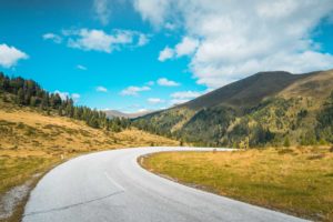 Curving road through a scenic mountainous landscape under a bright blue sky.