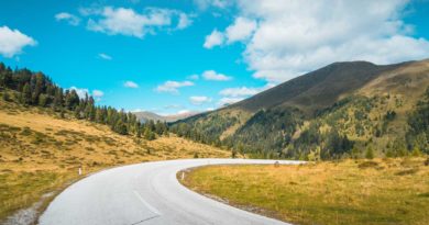 Curving road through a scenic mountainous landscape under a bright blue sky.