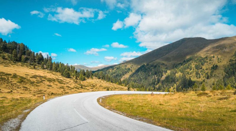 Curving road through a scenic mountainous landscape under a bright blue sky.