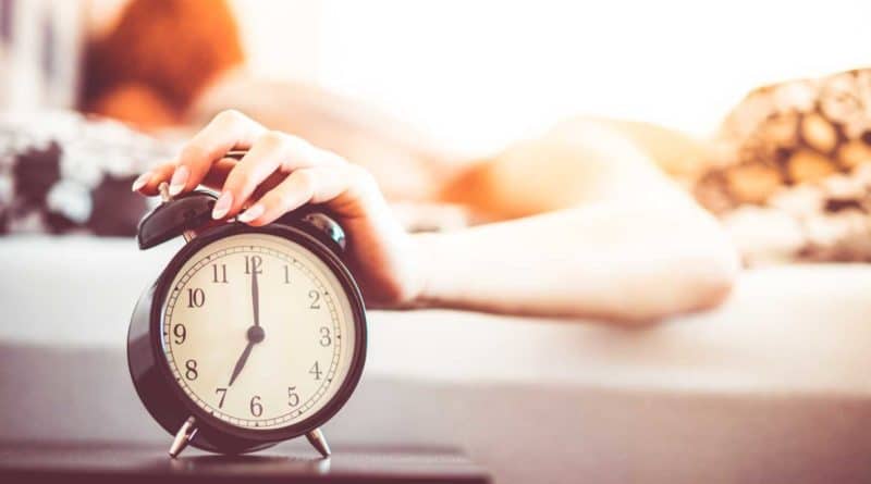 Person reaching to turn off an alarm clock in the morning.