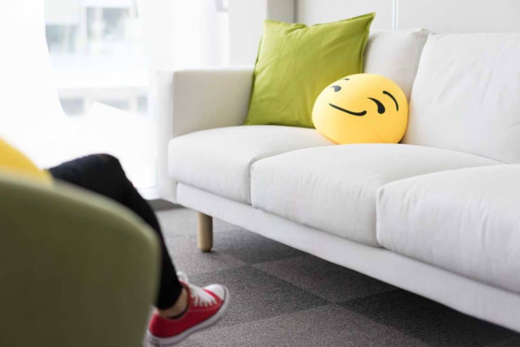 White sofa with a green pillow and a smiling emoji cushion in a bright room.