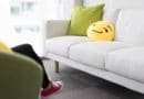White sofa with a green pillow and a smiling emoji cushion in a bright room.
