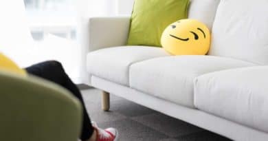 White sofa with a green pillow and a smiling emoji cushion in a bright room.